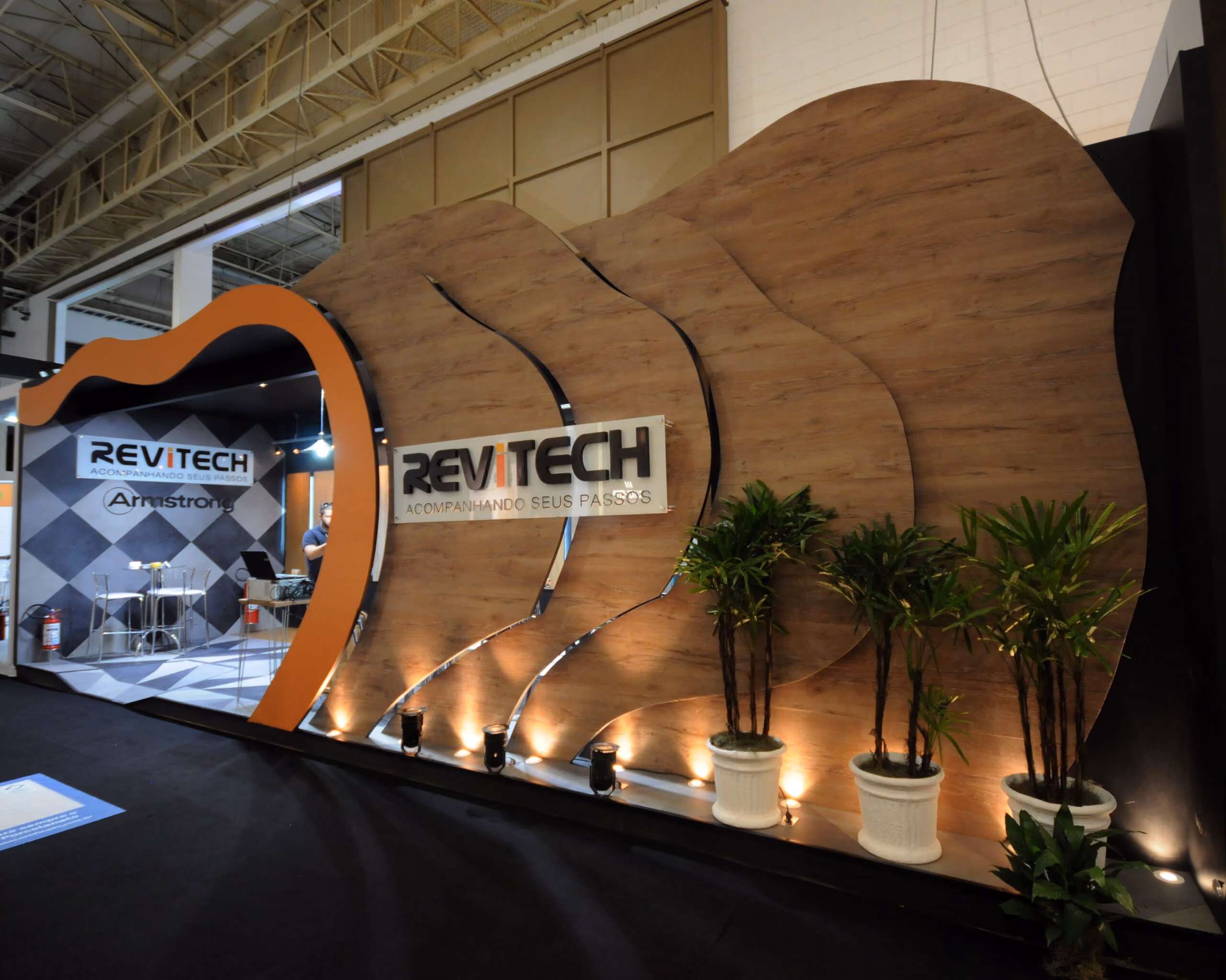 Estande da Revitech com decoração em madeira, plantas em vasos e área de atendimento interna.