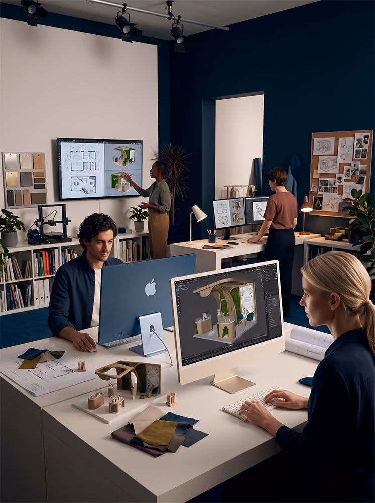 Quatro arquitetos trabalhando em modelos e plantas de design em computadores em um escritório moderno.